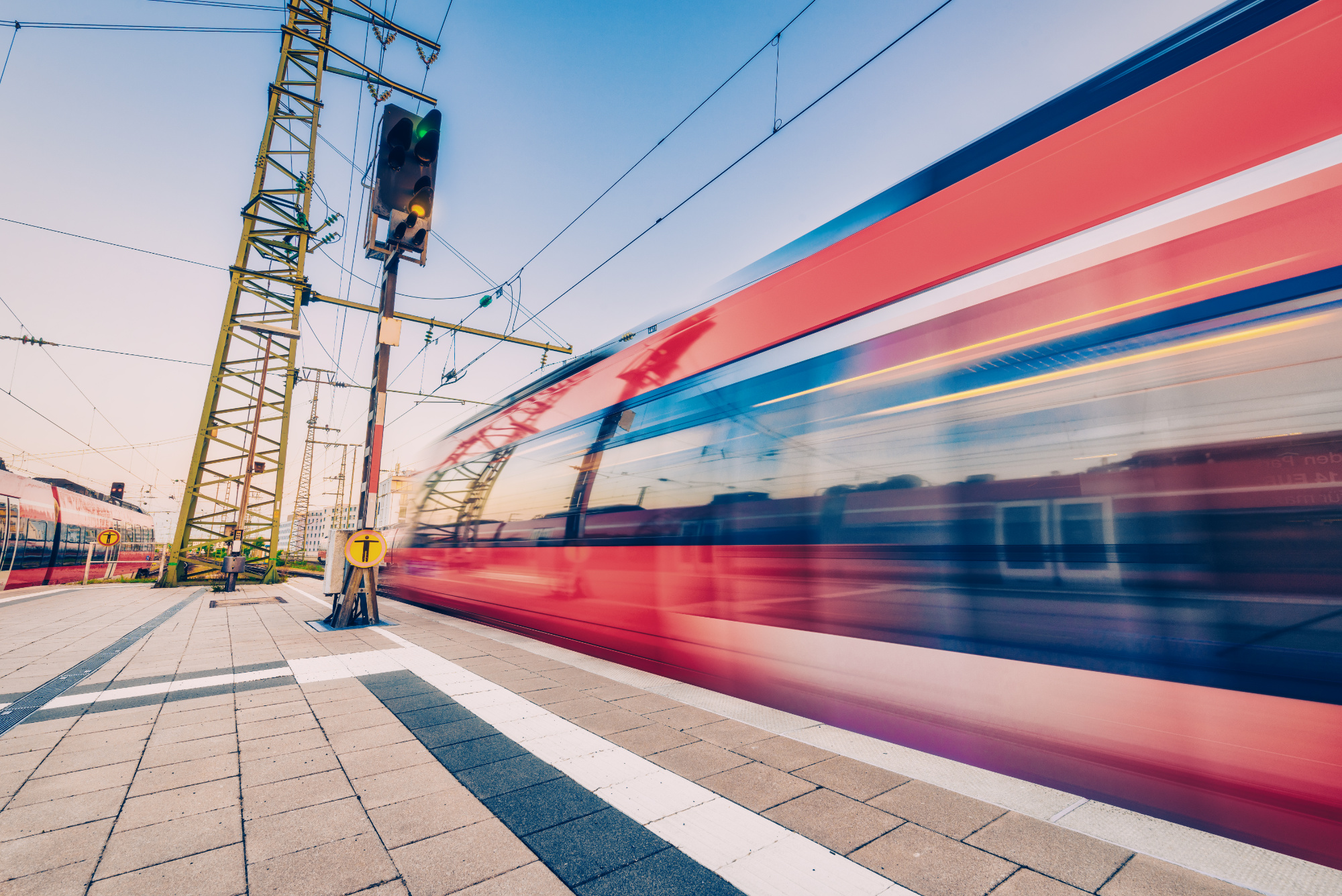 High speed train in motion on the railway station at sunset. Red blurred modern intercity train on the railway platform in Europe. Passenger railway transportation. Railroad in the evening. Travel